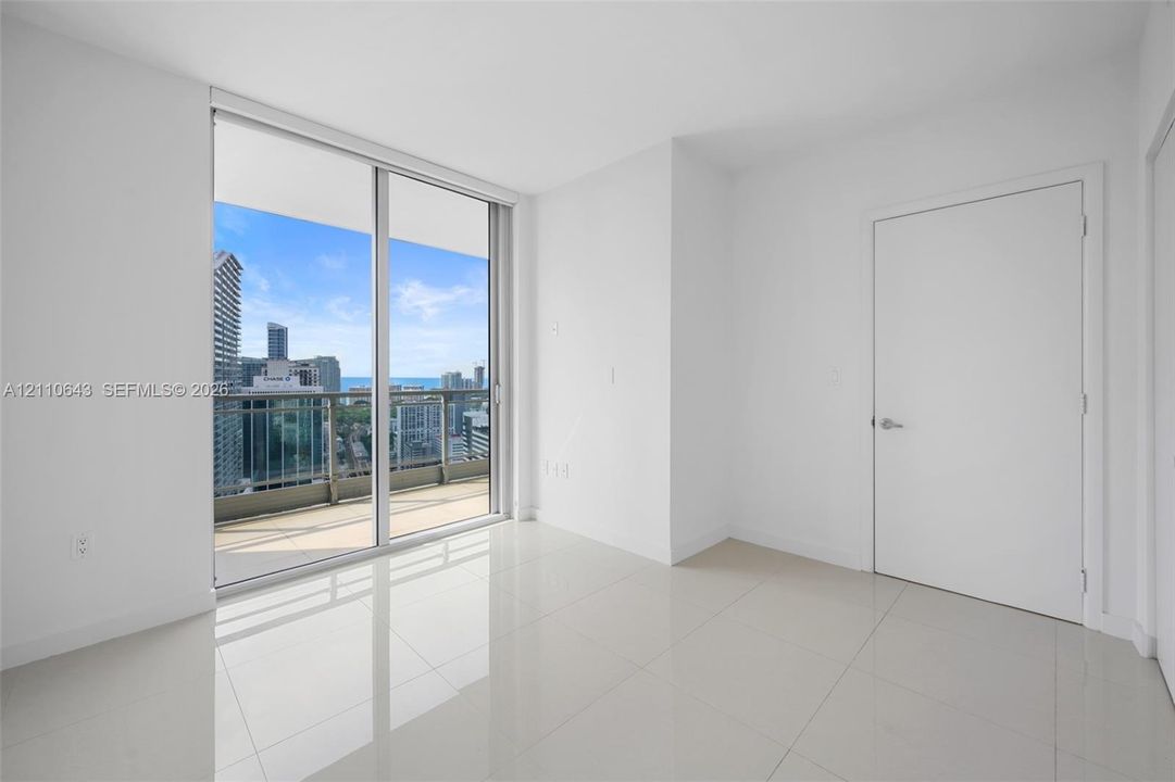 Floor-to-ceiling sliding glass doors, private balcony, polished tile flooring, and urban cityscape backdrop