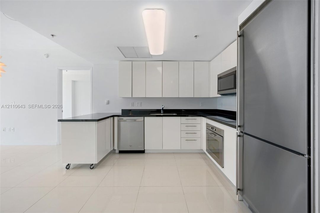 Kitchen featuring white flat-panel cabinetry, dark stone countertops, stainless steel appliances, and tile flooring