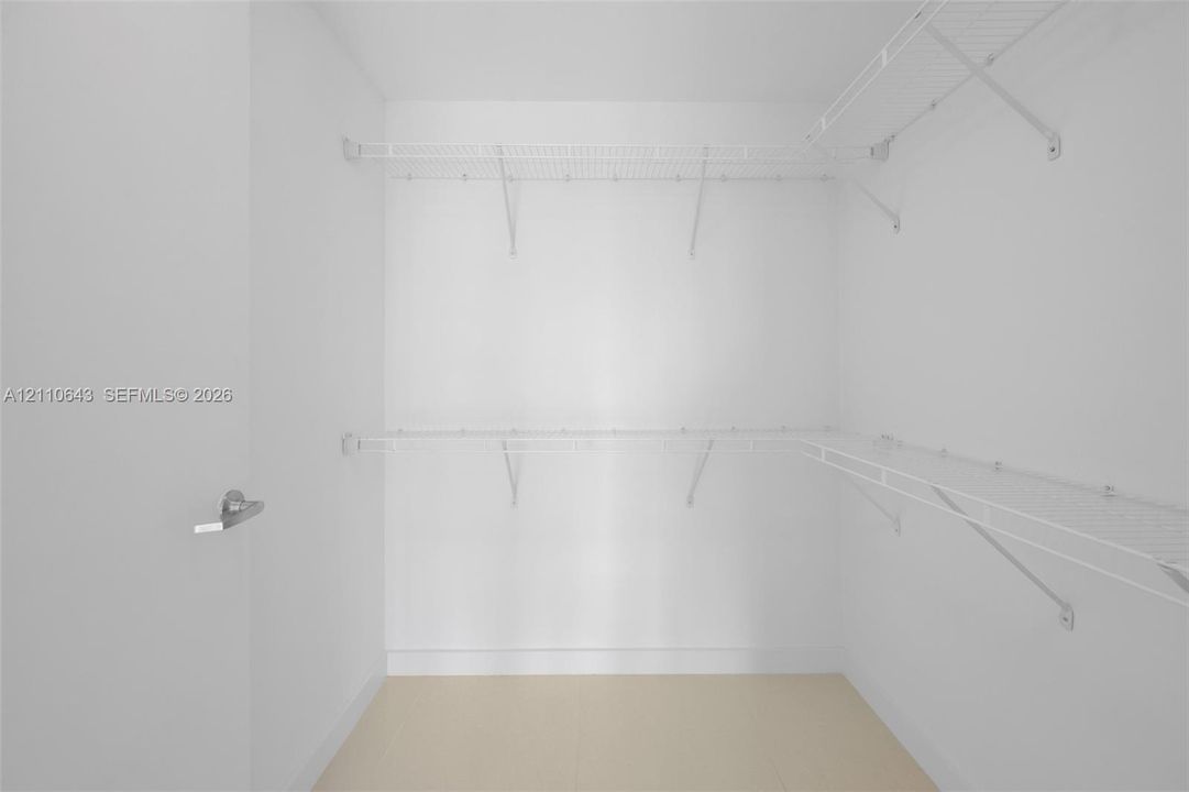 Storage closet featuring two levels of white wire shelving and a metal lever handle