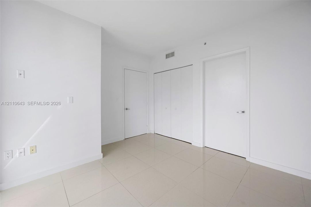 Neutral interior space featuring polished tile flooring, smooth wall finishes, two interior doors, and a double-door reach-in closet
