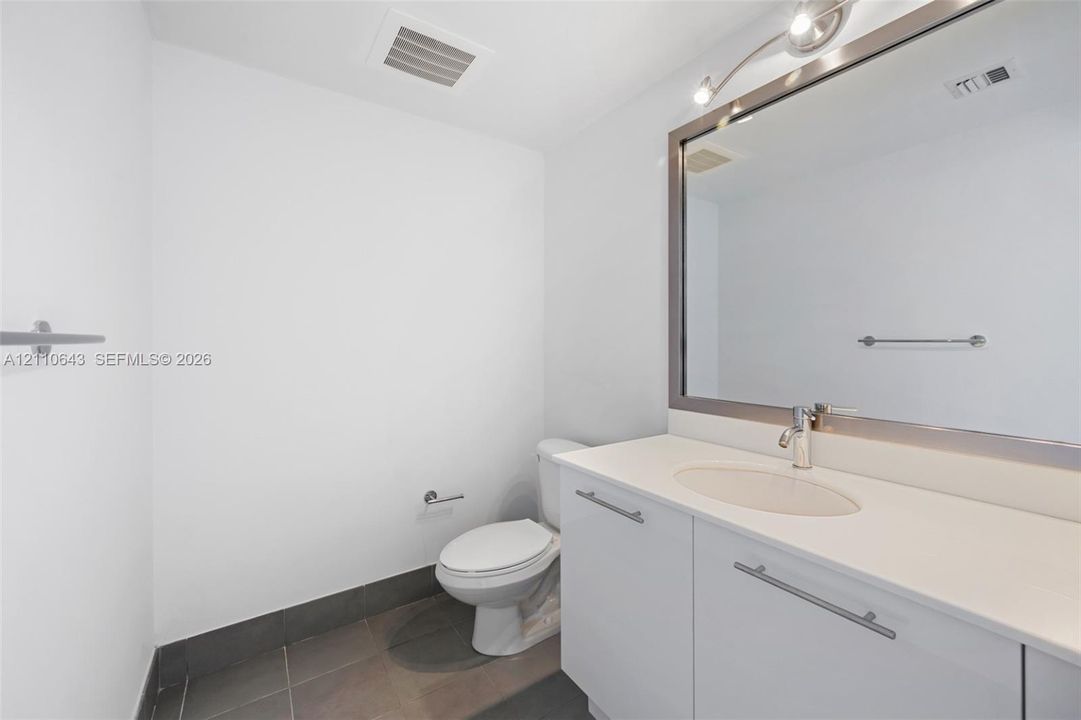 Bathroom featuring a white vanity with a composite countertop, undermount sink, brushed nickel faucet, large wall-mounted mirror, and tile flooring