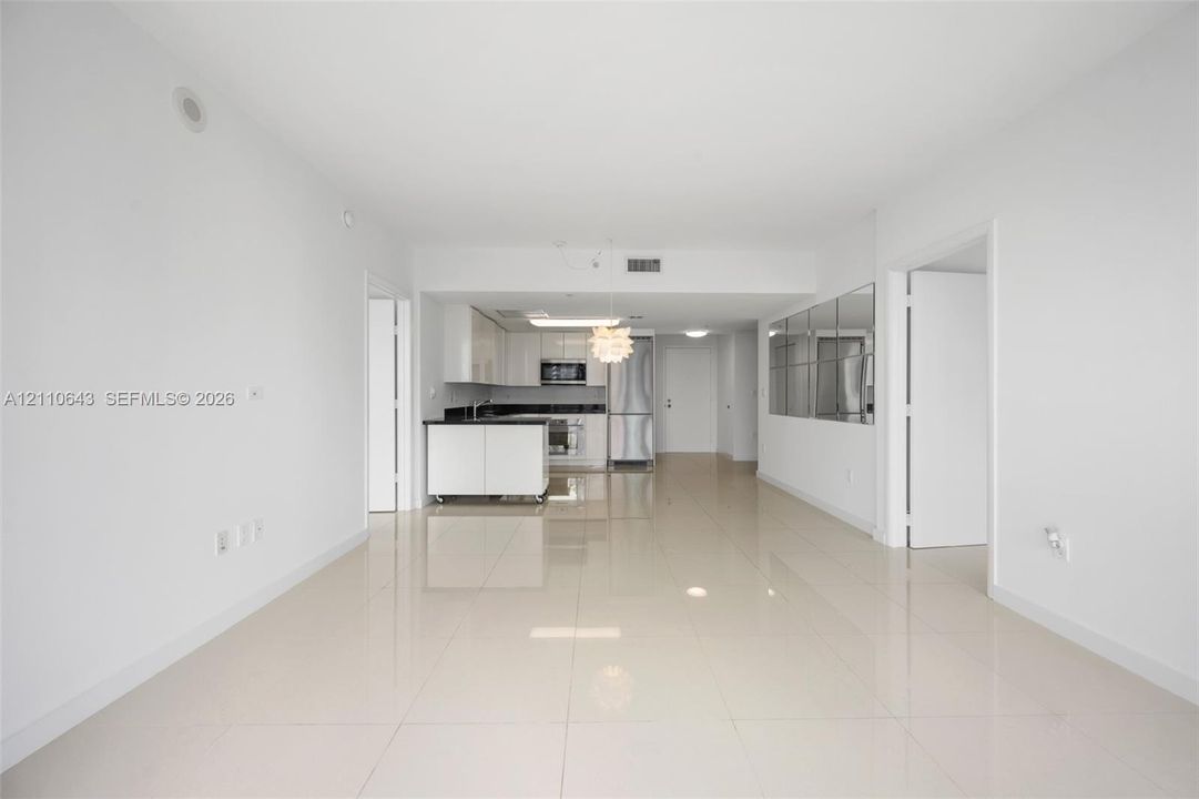 Open-concept interior featuring large-format tile flooring, white gloss cabinetry, stone countertops, stainless steel appliances, and a wall-mounted mirrored panel