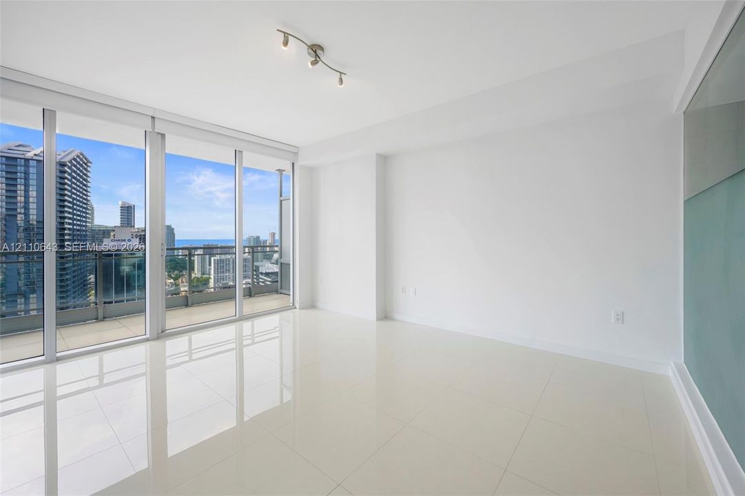 Floor-to-ceiling sliding glass doors, private balcony, polished tile flooring, and integrated track lighting