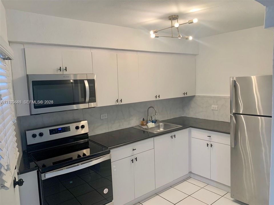 Kitchen featuring white cabinetry, dark countertops, stainless steel appliances, a tile backsplash, and an overhead multi-light fixture