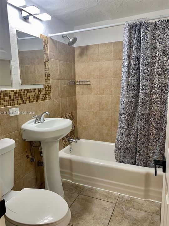 Pedestal sink with chrome faucet, shower-tub combination, ceramic wall tile surround with mosaic tile accents, and tiled flooring