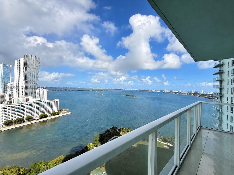 Covered balcony featuring tile flooring and a glass-paneled railing overlooking the bay and urban skyline