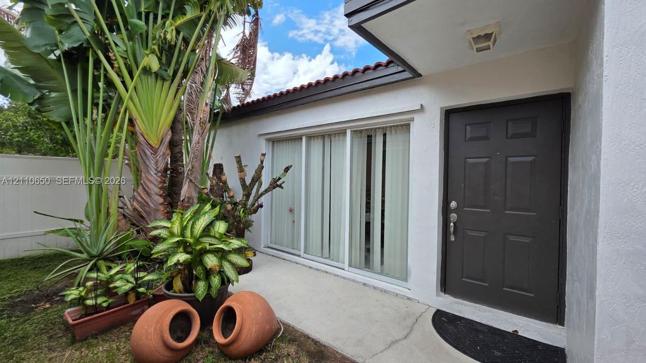 Exterior entryway featuring a white stucco facade, six-panel dark-finish entry door, sliding glass door, and a clay tile roofline