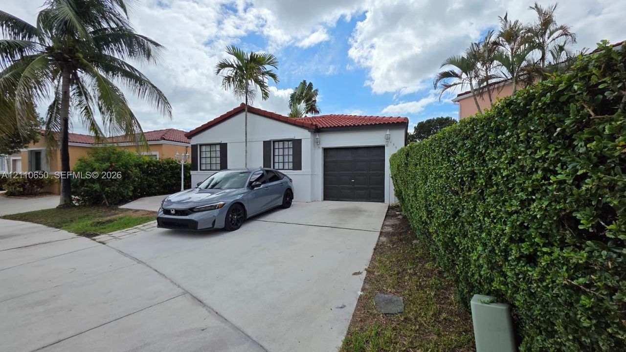 Stucco exterior featuring a red tile roof, dark shutters, an integrated one-car garage, and a concrete driveway