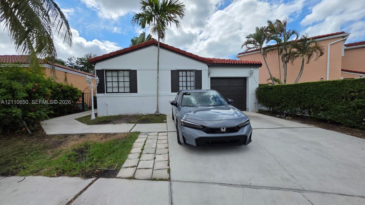 Single-story residence featuring a white stucco facade, red tile roof, multi-pane windows, and a paved driveway leading to an attached garage