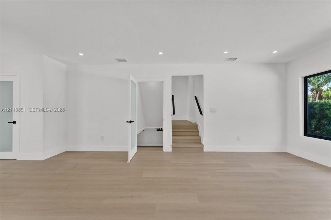 Neutral-toned interior space featuring wood-finish flooring, recessed lighting, frosted glass panel doors, and a large window with black framing
