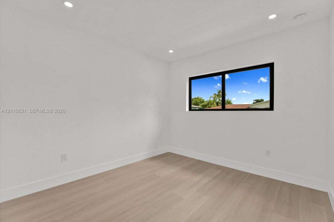 Interior space featuring neutral wall paint, wood-finish flooring, recessed ceiling lighting, and a window with a black frame