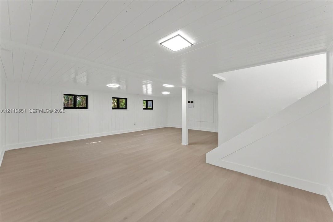 Finished interior space featuring wood-finish flooring, white paneled walls, a painted wood-plank ceiling, square LED flush-mount lighting, and multi-pane windows with black frames