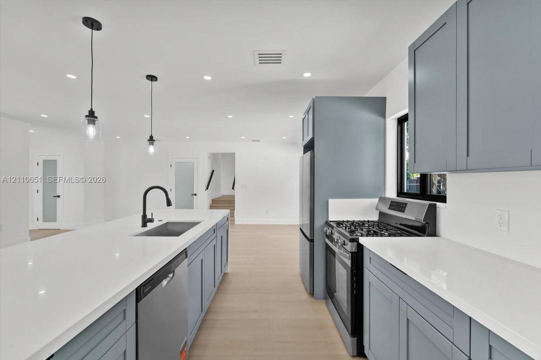 Kitchen featuring shaker-style cabinetry, quartz countertops, a central island with a matte black faucet, stainless steel appliances, and recessed lighting