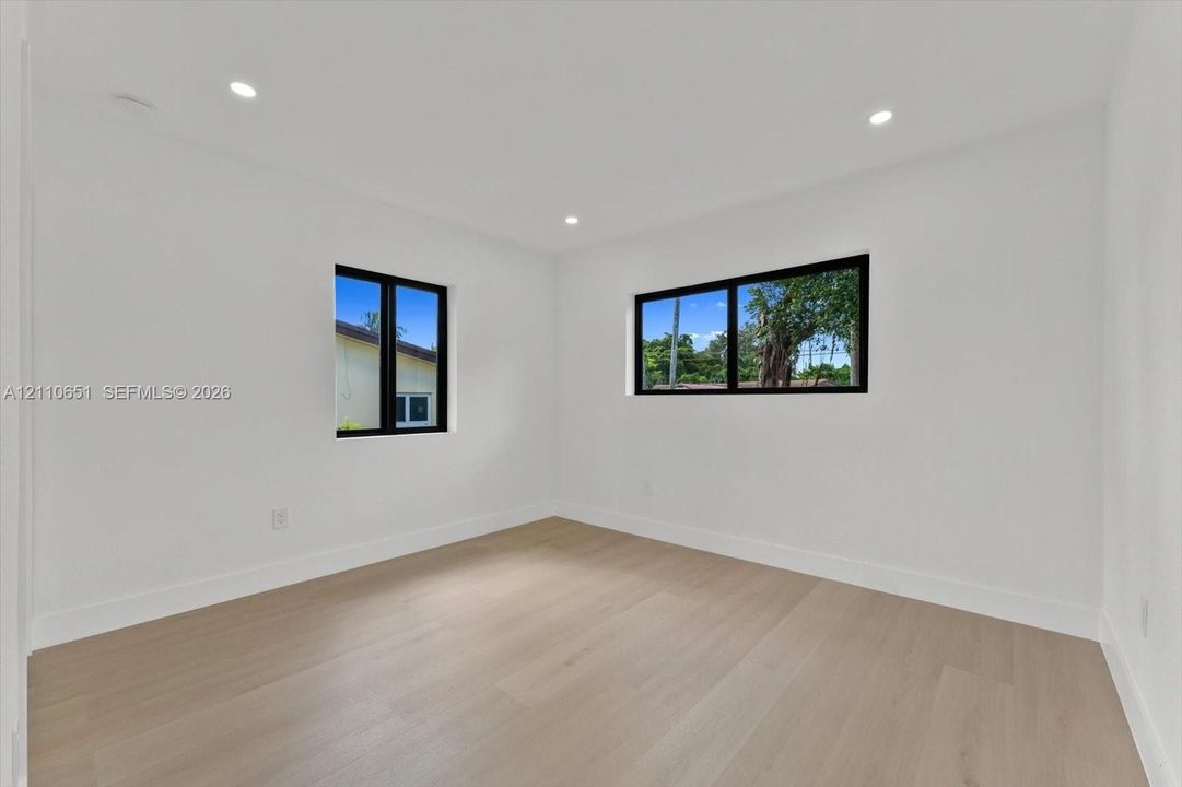 Neutral interior featuring wood-finish flooring, crisp white walls, recessed ceiling lighting, and black-framed windows