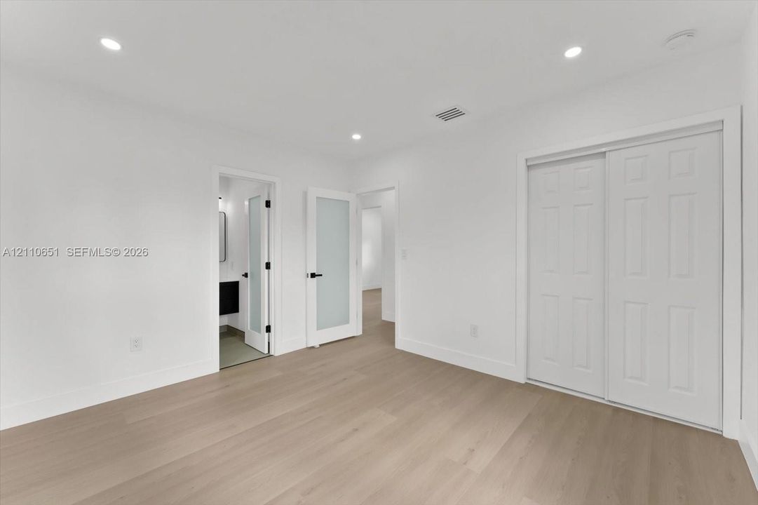 Interior room featuring wood-finish flooring, recessed lighting, frosted glass panel doors, and a double-door closet with six-panel detailing