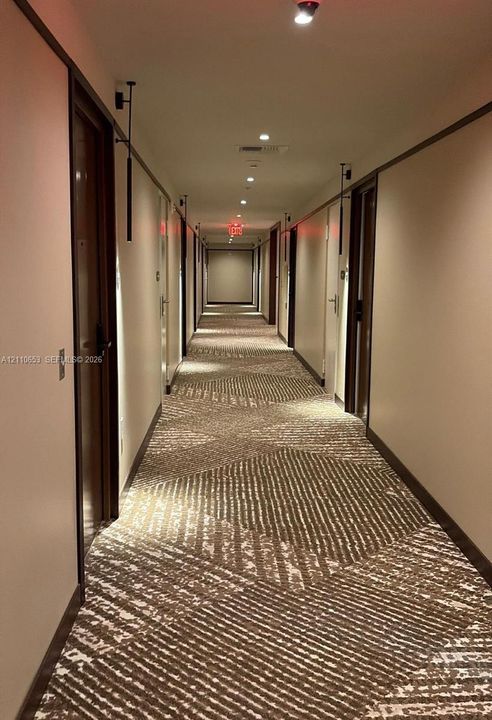 Hallway featuring geometric patterned carpeting, recessed ceiling lighting, wall-mounted sconces, and wooden door frames