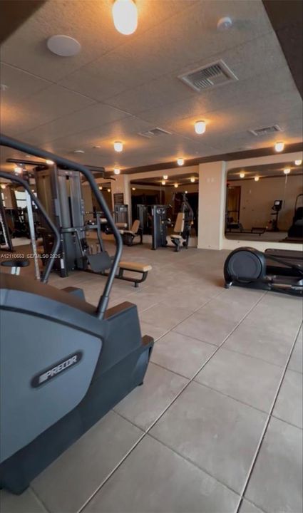 Large-scale exercise facility featuring expansive mirrored wall panels, neutral oversized floor tiling, and recessed ceiling lighting