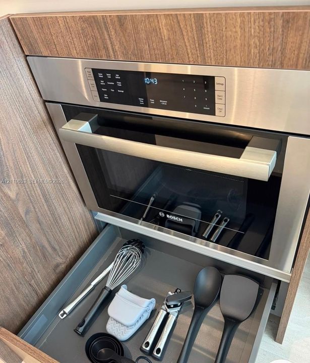 Built-in stainless steel microwave oven with digital display, integrated into wood-finish cabinetry featuring a pull-out drawer