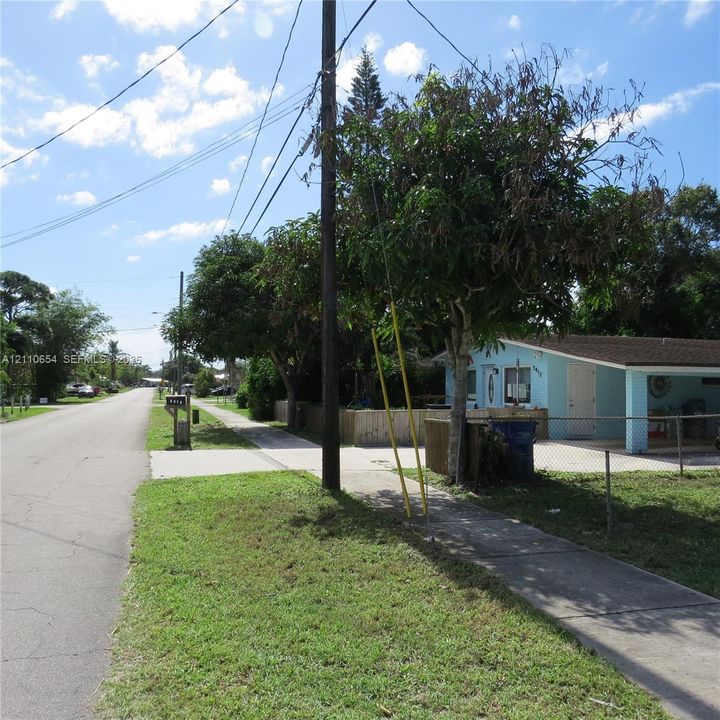 Single-story exterior featuring a light blue stucco finish, a covered carport, and perimeter chain-link fencing