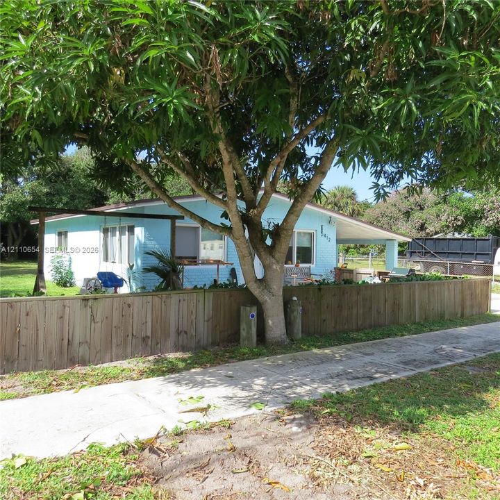 Exterior facade featuring painted brick masonry, a covered carport, and a perimeter wooden privacy fence