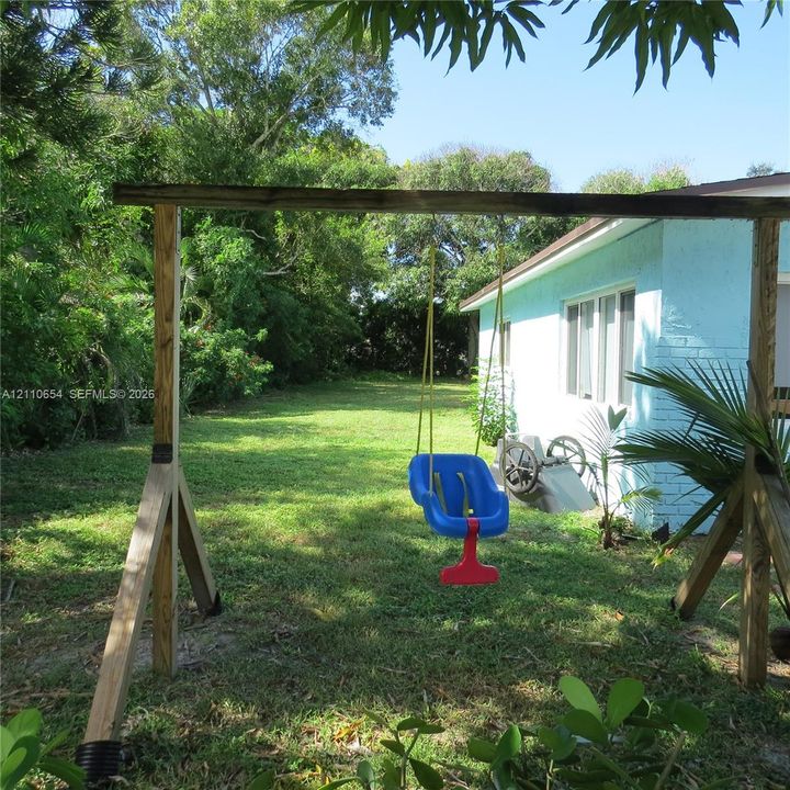 Backyard featuring a grass lawn, mature perimeter trees, and a painted masonry exterior