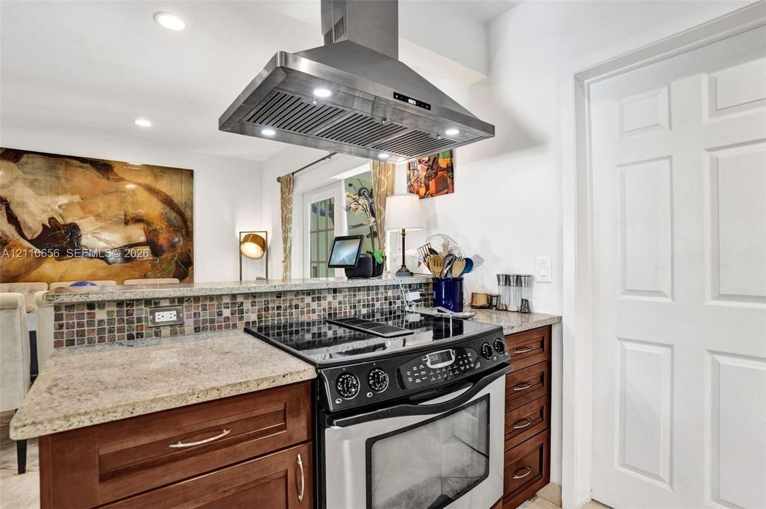 Kitchen featuring wood cabinetry, stone countertops, a mosaic tile backsplash, a stainless steel range, and a stainless steel range hood