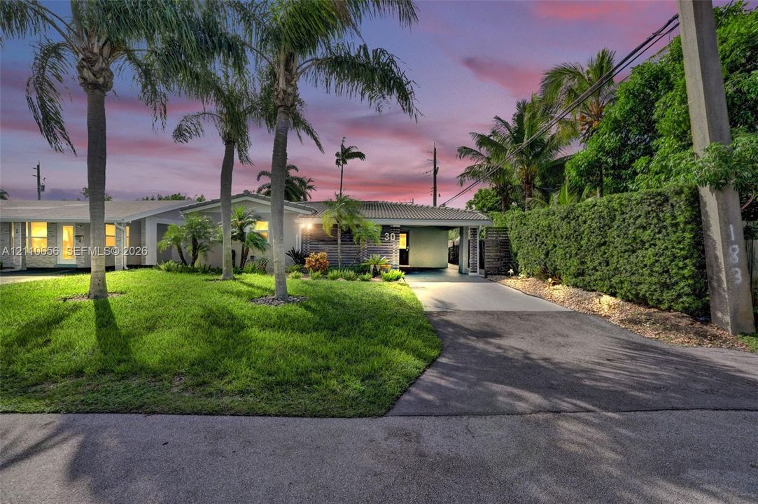 Single-story exterior featuring a concrete tile roof, attached covered carport, paved driveway, and mature landscaping