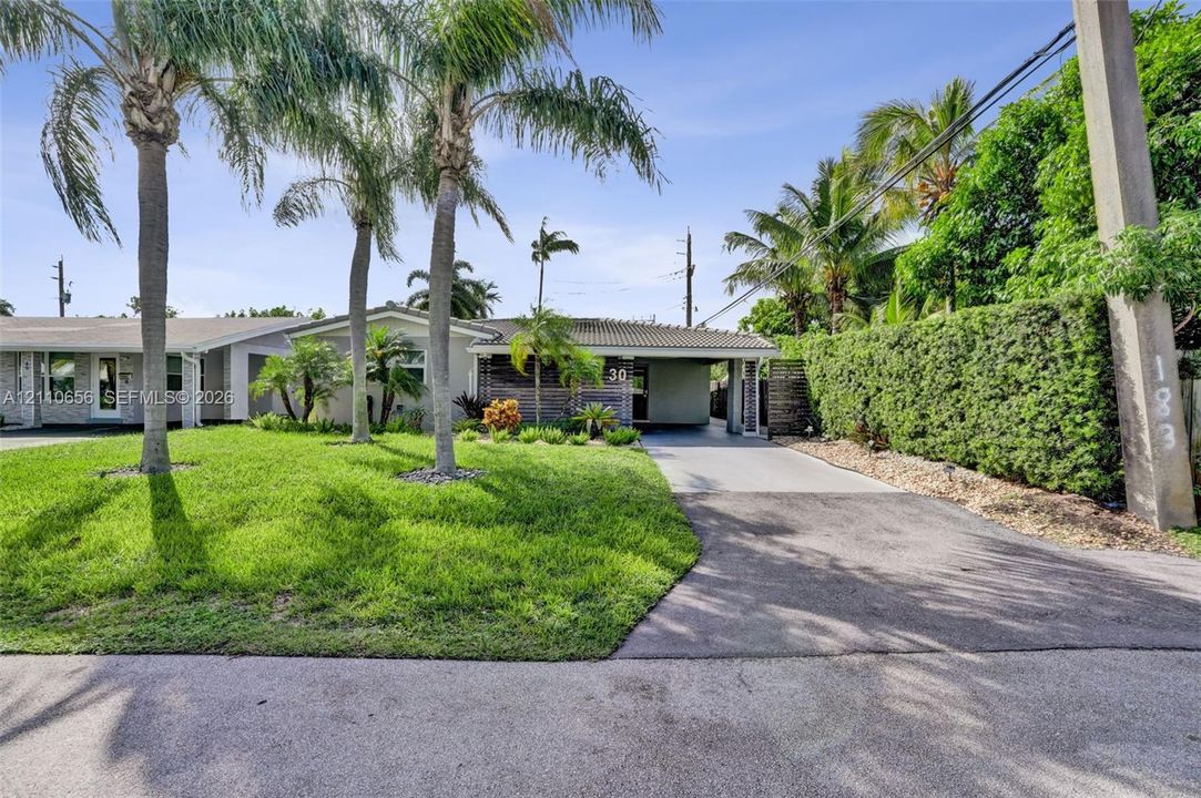 Exterior featuring a concrete tile roof, paved driveway with an integrated carport, established palm trees, and manicured landscaping