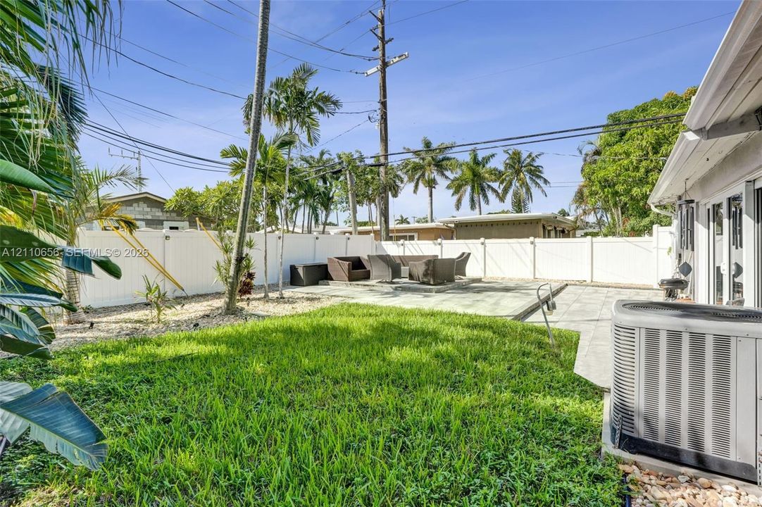 Backyard featuring a paved patio area, manicured lawn, stone landscape accents, and a perimeter vinyl privacy fence
