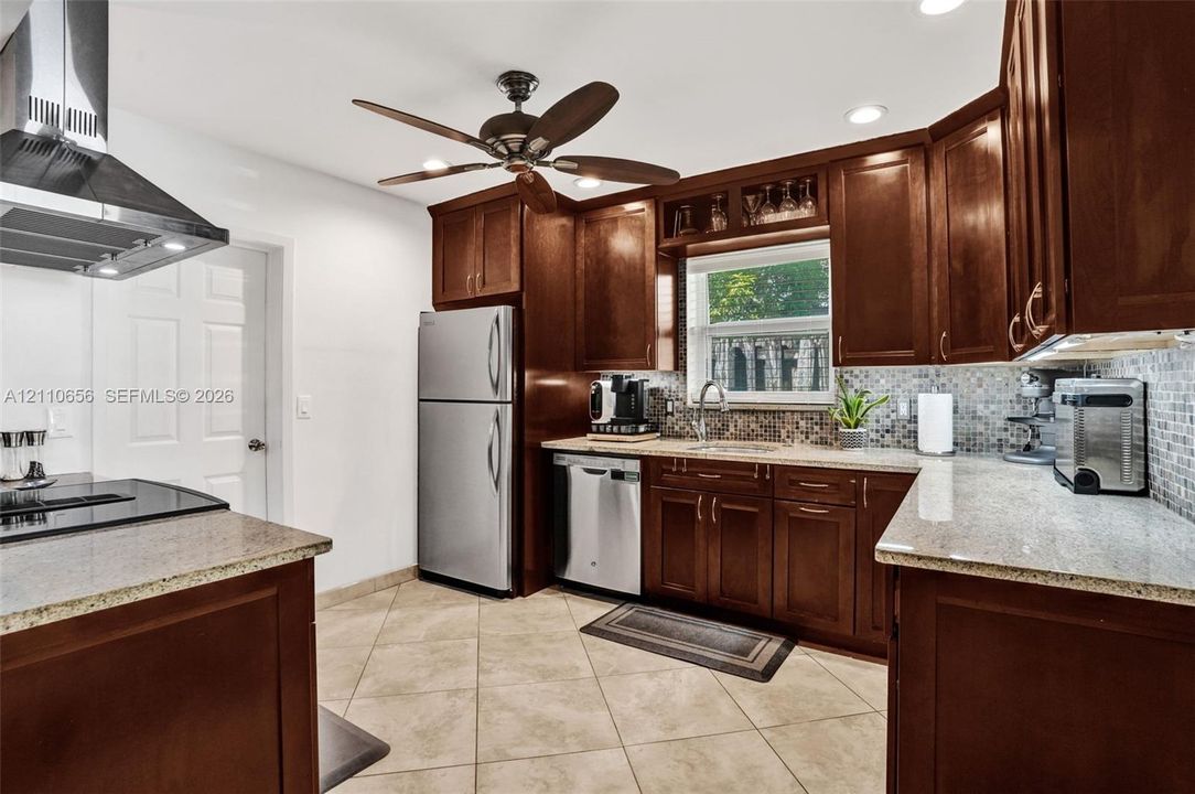 Kitchen featuring dark wood cabinetry, stone countertops, stainless steel appliances, a mosaic tile backsplash, and ceramic tile flooring
