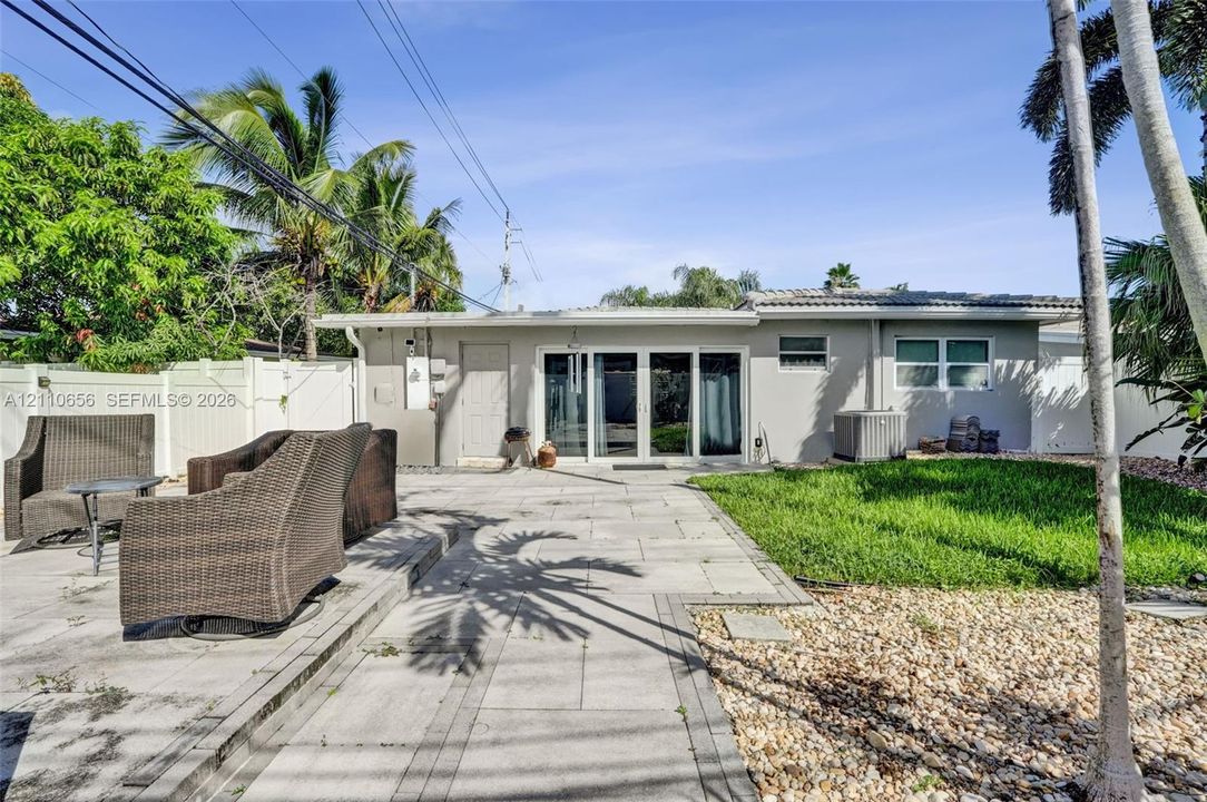 Rear exterior featuring a concrete paver patio, sliding glass doors, a manicured lawn, and perimeter vinyl fencing
