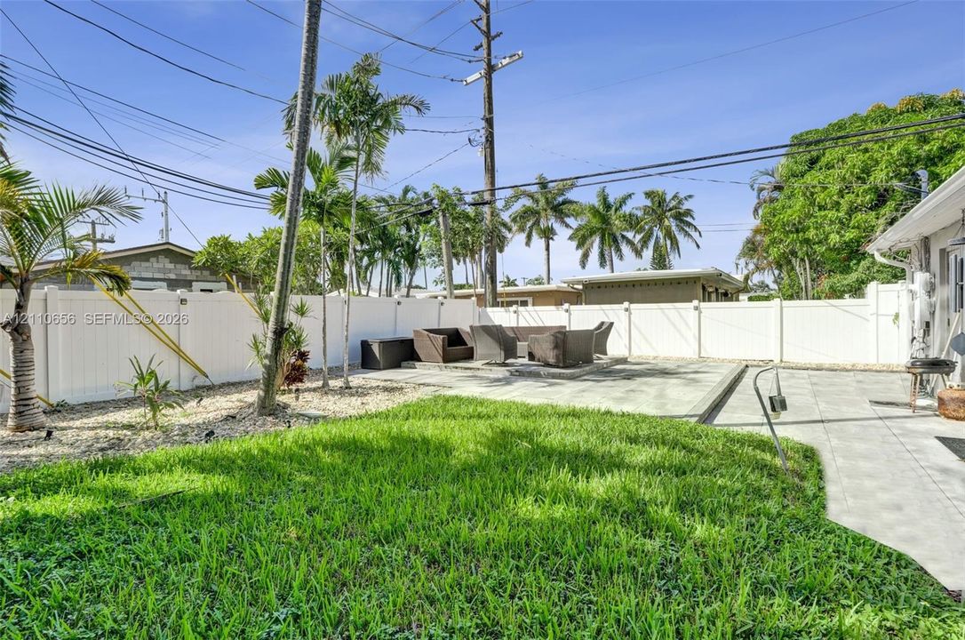 Backyard featuring a paved patio, manicured lawn, white vinyl perimeter fencing, and mature palm trees