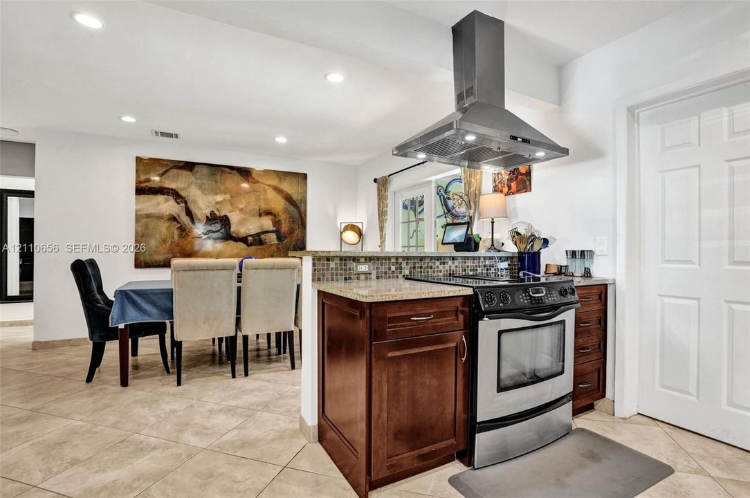 Kitchen featuring dark wood cabinetry, stone-finish countertops, mosaic tile backsplash, stainless steel range, and stainless steel chimney-style range hood