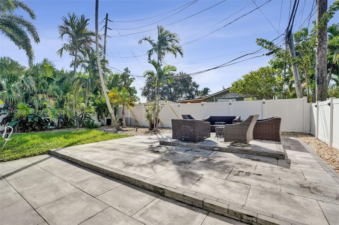 Backyard featuring a tiered stone paver patio, white vinyl privacy fencing, mature palm trees, and established landscaping