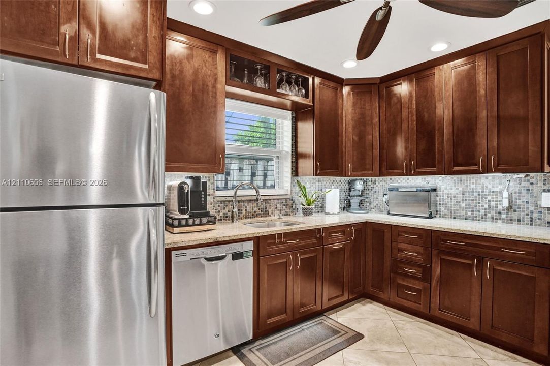 Kitchen featuring raised-panel wood cabinetry, glass-front upper cabinet detailing, stainless steel appliances, stone-look countertops, and a multi-tonal mosaic tile backsplash
