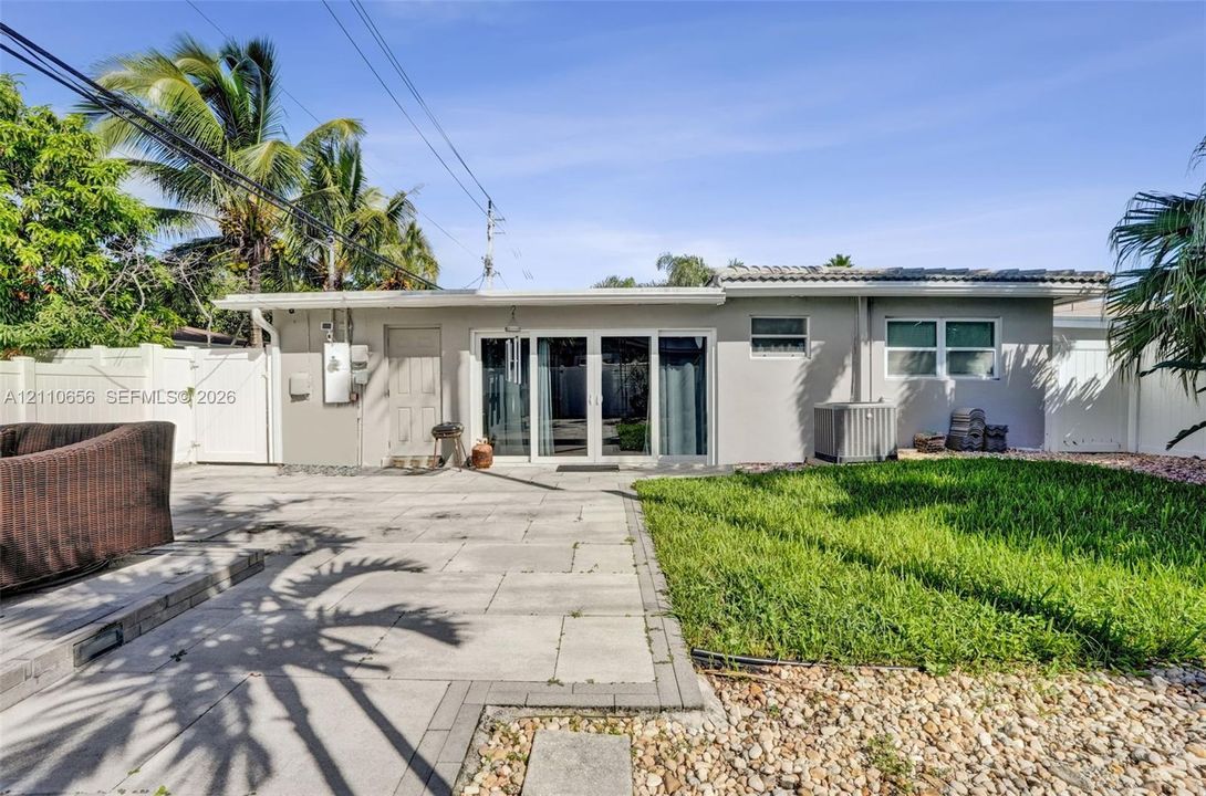 Rear exterior featuring a concrete paver patio, a fenced lawn, and multi-panel sliding glass doors