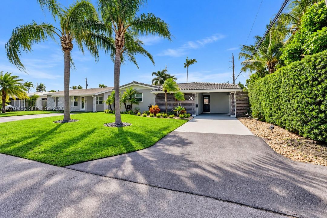 Single-story residence featuring a paved driveway, covered entryway, mature palm trees, and manicured landscaping