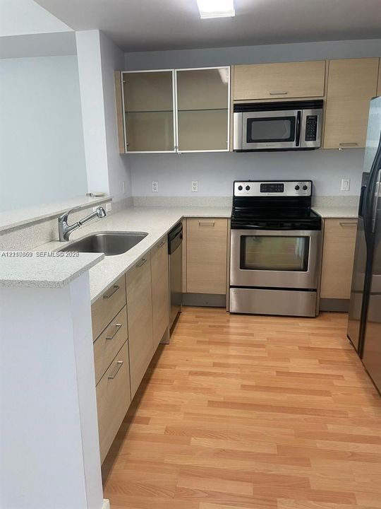 Kitchen featuring light-finish cabinetry with glass-front uppers, stainless steel appliances, speckled solid-surface countertops, and wood-finish flooring