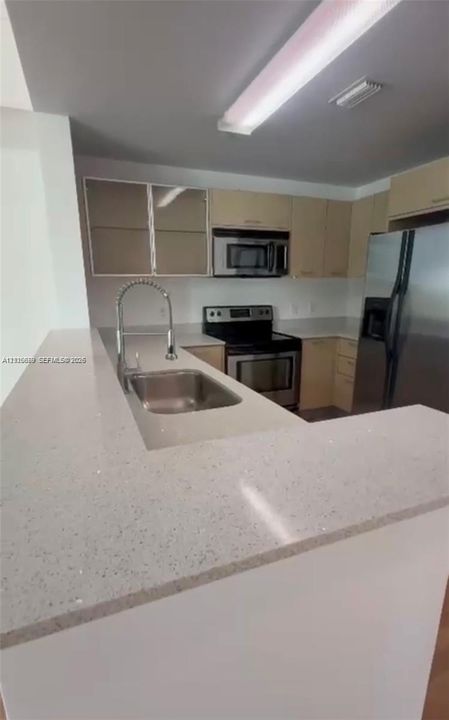 Kitchen featuring stone-finish countertops, stainless steel appliances, flat-panel cabinetry, a stainless steel undermount sink, and a high-arch pull-down faucet