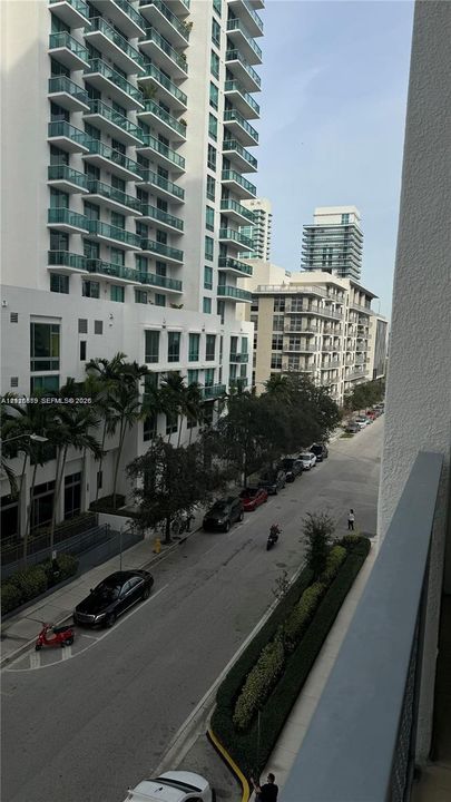 Elevated balcony with a solid metal railing overlooking a paved street and multi-story urban architecture