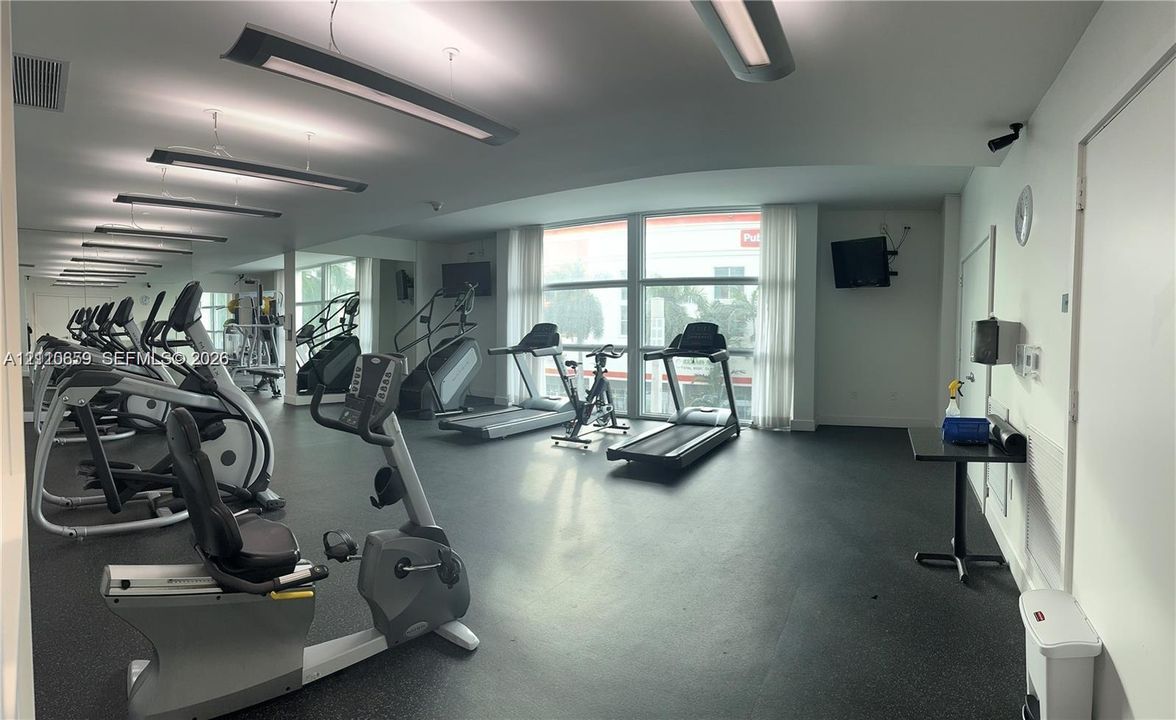 Fitness center featuring rubber flooring, floor-to-ceiling windows, wall-to-wall mirrors, and linear recessed lighting