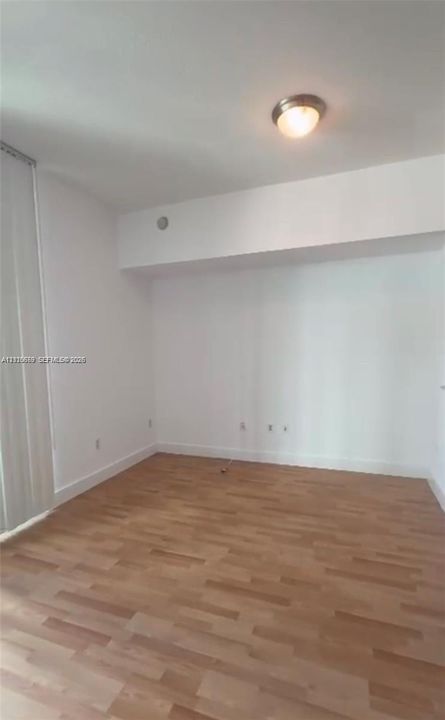 Interior room featuring wood-finish flooring, white walls, vertical blinds, and a flush-mount ceiling light fixture