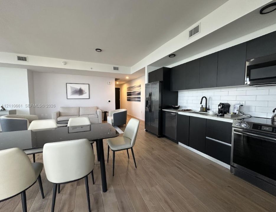 Kitchen featuring matte black flat-panel cabinetry, white subway tile backsplash, stainless steel appliances, and wood-finish flooring