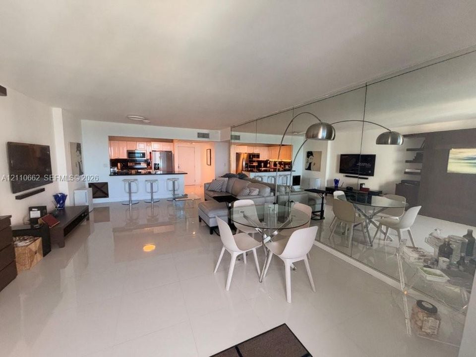 Open-concept living space featuring high-gloss tile flooring, floor-to-ceiling wall mirror, recessed lighting, and kitchen with breakfast bar and built-in cabinetry