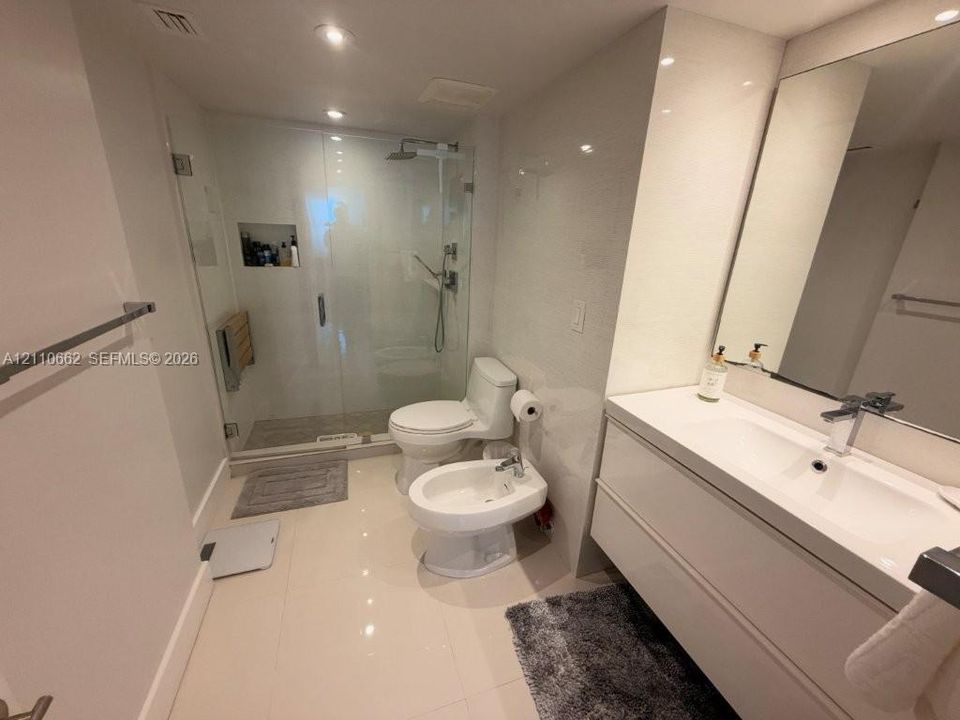 Modern bathroom featuring a wall-mounted floating vanity with integrated basin, glass-enclosed shower with wall-integrated shelving, bidet, and polished tile flooring