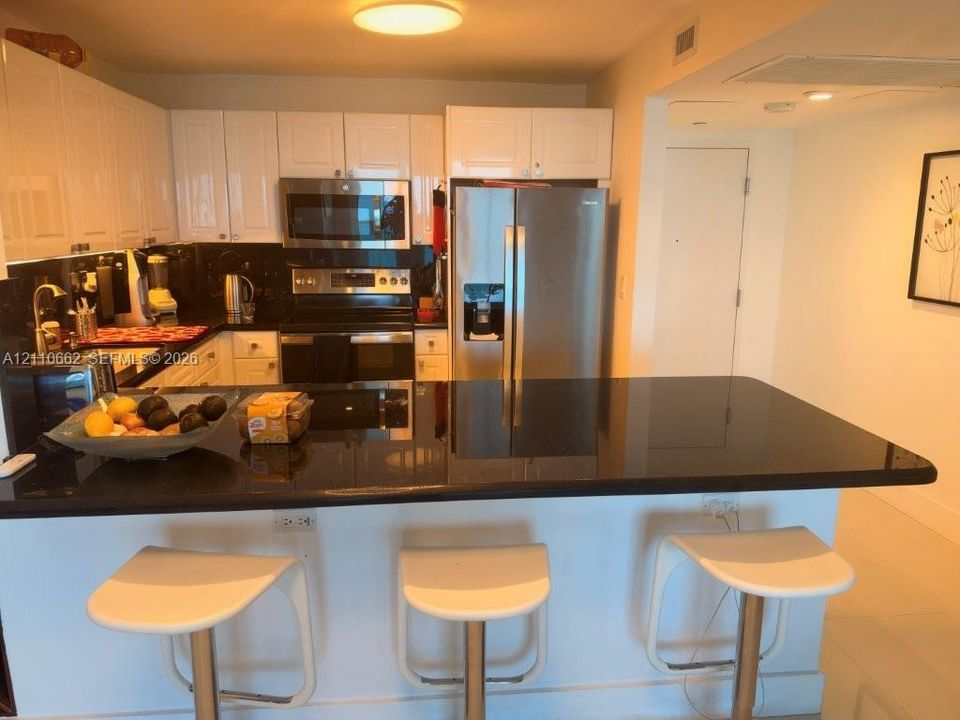 Kitchen featuring white cabinetry, black stone countertops, stainless steel appliances, and a breakfast bar