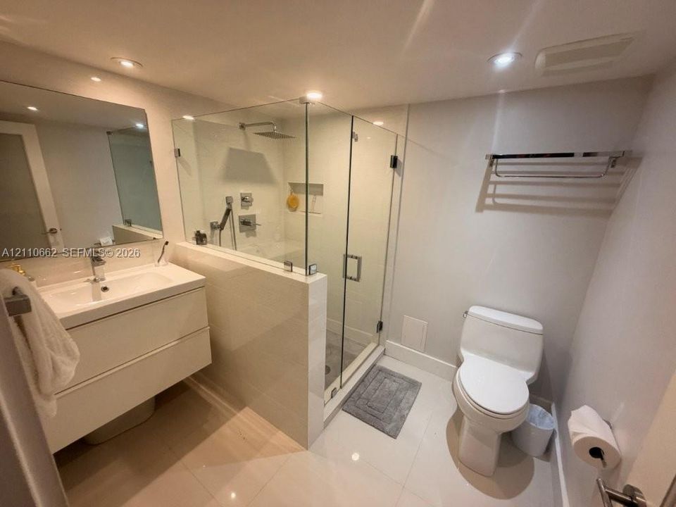 Bathroom featuring a floating white vanity with integrated sink, walk-in glass-enclosed shower with rainfall showerhead, and recessed ceiling lighting