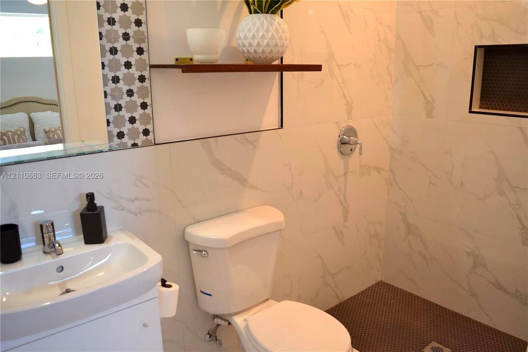 Bathroom featuring large-format stone-patterned wall tile, walk-in shower with recessed niche, integrated vanity with polished chrome faucet, decorative geometric accent tiling, and built-in wall shelving