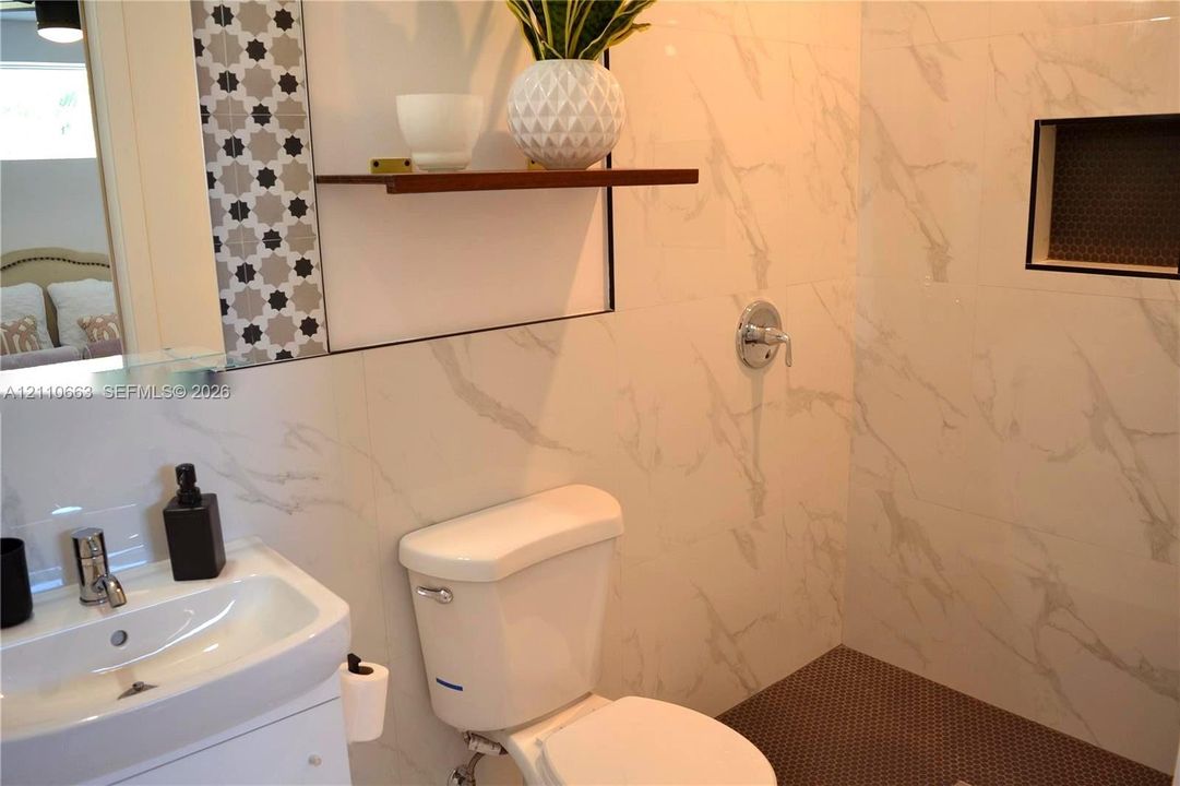 Bathroom featuring large-format wall tile with a veined pattern, built-in shower niche, floating wood-finish shelf, geometric-patterned tile backsplash, and a pedestal sink with chrome faucet hardware