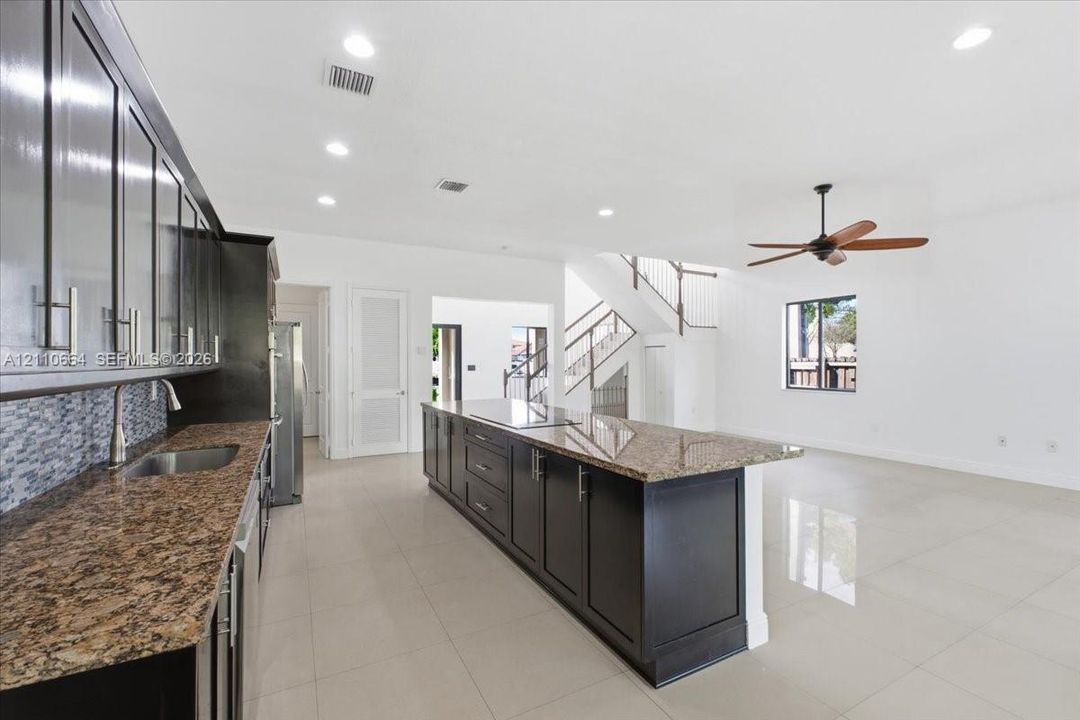 Spacious kitchen with a generous center island housing a new induction cooktop, granite countertops, rich dark cabinetry, double wall ovens, stainless steel refrigerator and dishwasher, recessed lighting, and tile flooring